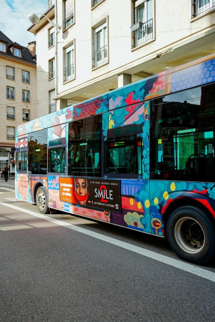 Vibrant city bus with artistic design on an urban street featuring colorful graffiti and advertisement.